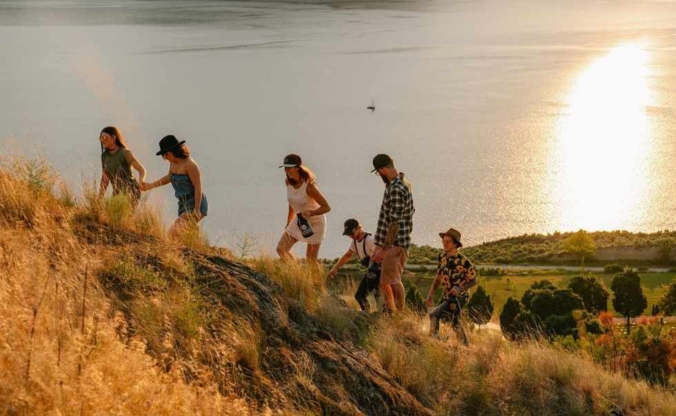 6 people climb a hill overlooking a lake during sunset.