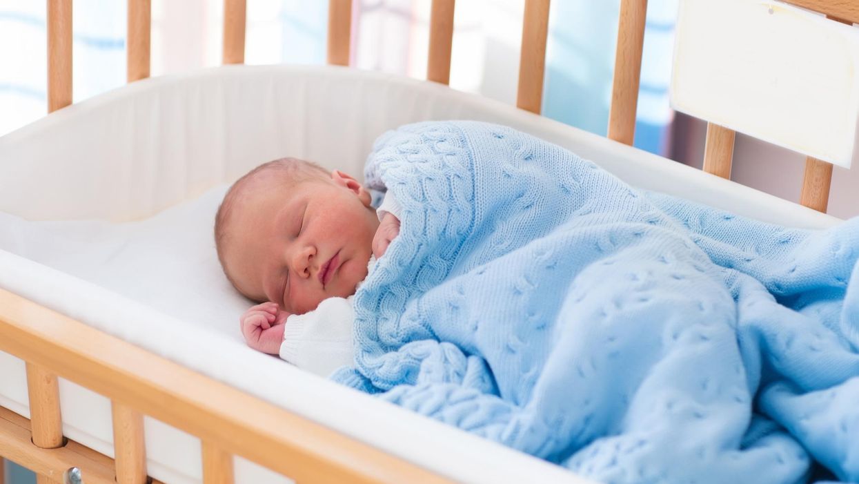 A baby sleeping in a cot, with a blue blanket on top of them.