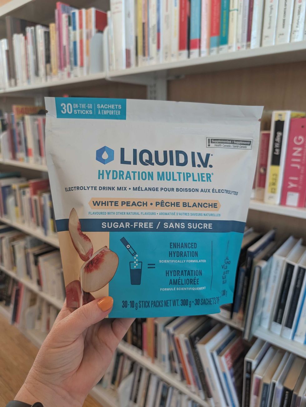 A bag of Liquid I.V. Sugar-Free White Peach is shown in front of a row of library books.