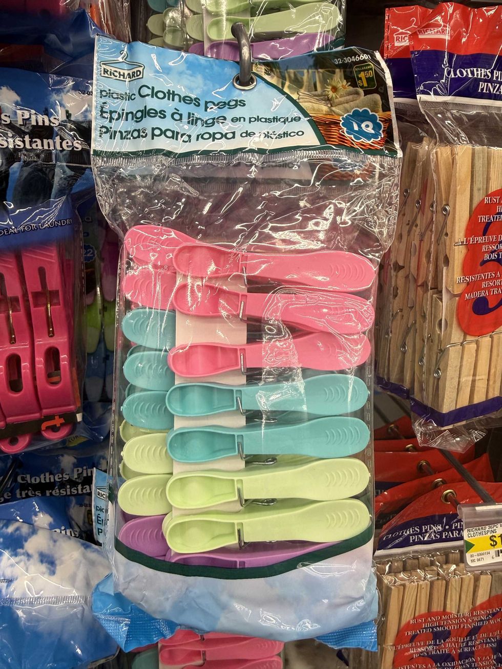 A bag of multi-coloured plastic clothes pegs hanging on a store shelf.