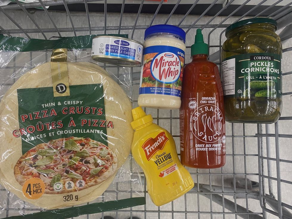 A bag of thin and crispy pizza crust wraps, Miracle Whip, a yellow tube of French's mustard, bottle of red Sriracha sauce, a jar of pickles and can of tuna in a shopping cart.