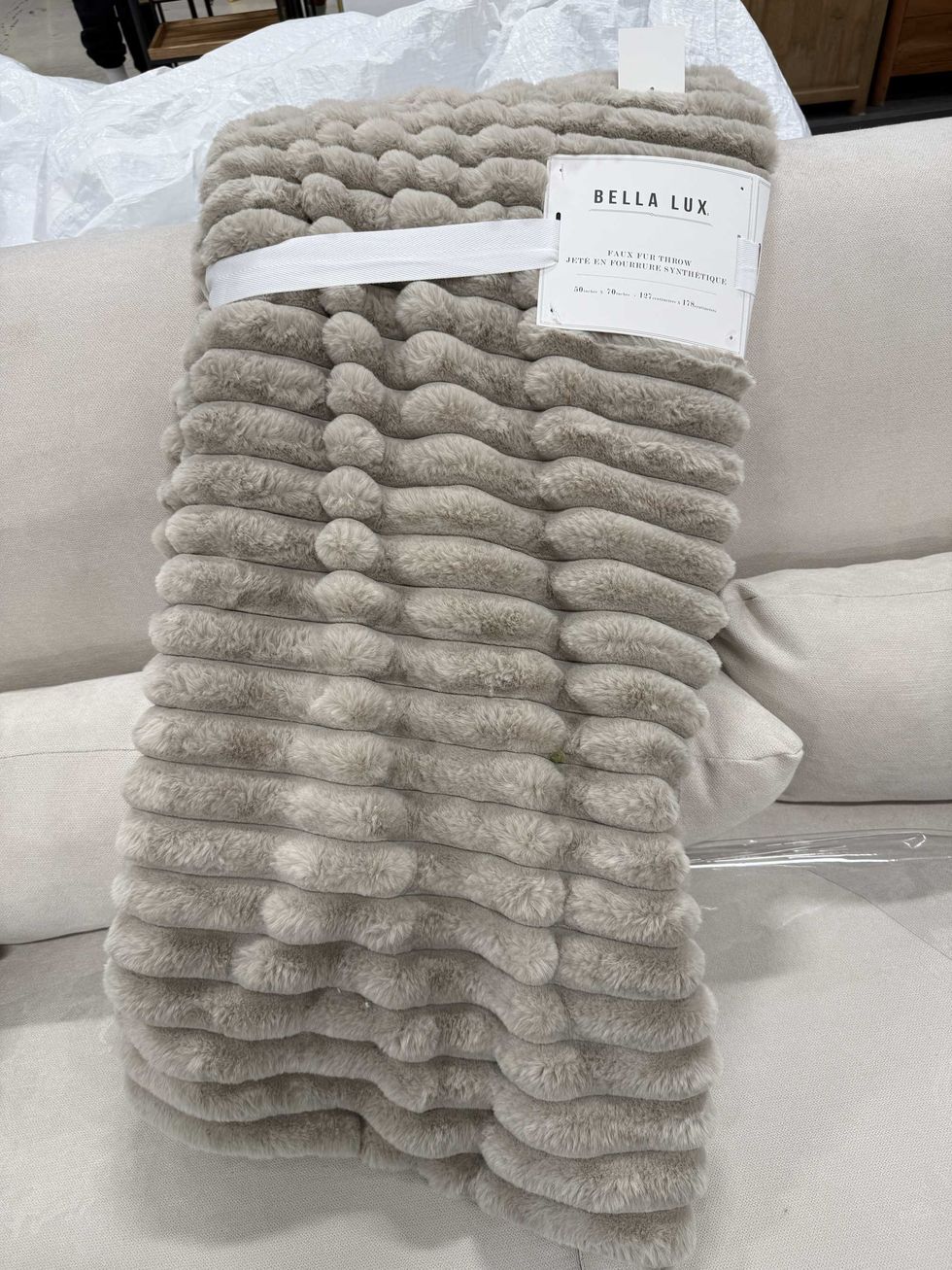 A beige faux fur blanket on a couch inside a store.