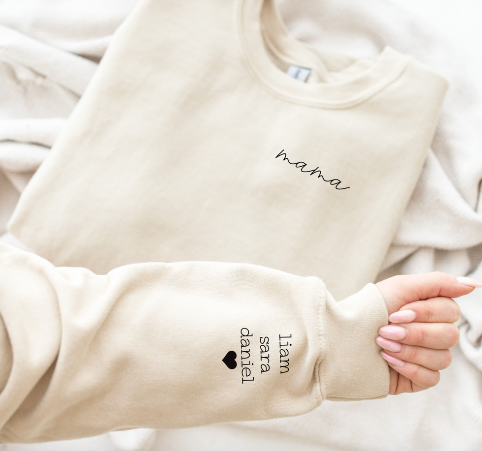 A beige sweater that says "mama" on the front" and three names on the sleeves along with a heart.