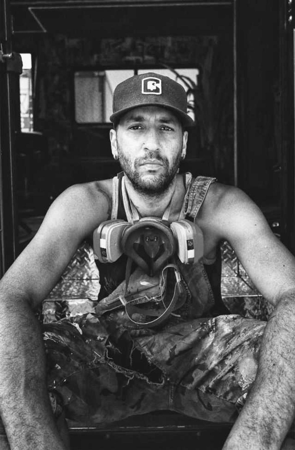 A black and white portrait of Paul Glyn-Williams with a respirator mask hanging around his neck.