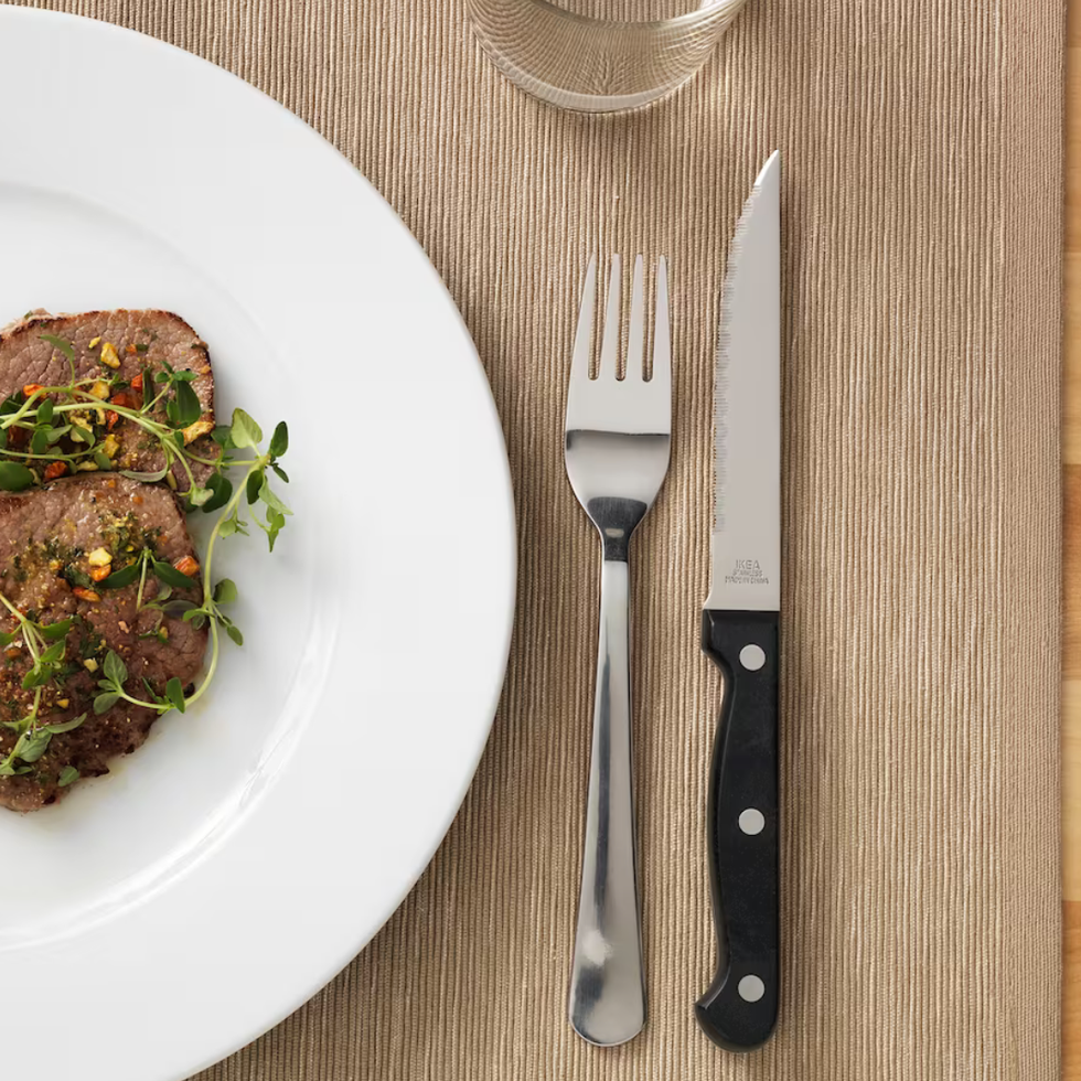 A black-handled steak knife next to a fork and plate of food.