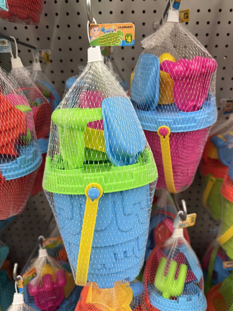 A blue, green and yellow bucket filled with shovels and other beach toys hanging on a store shelf.