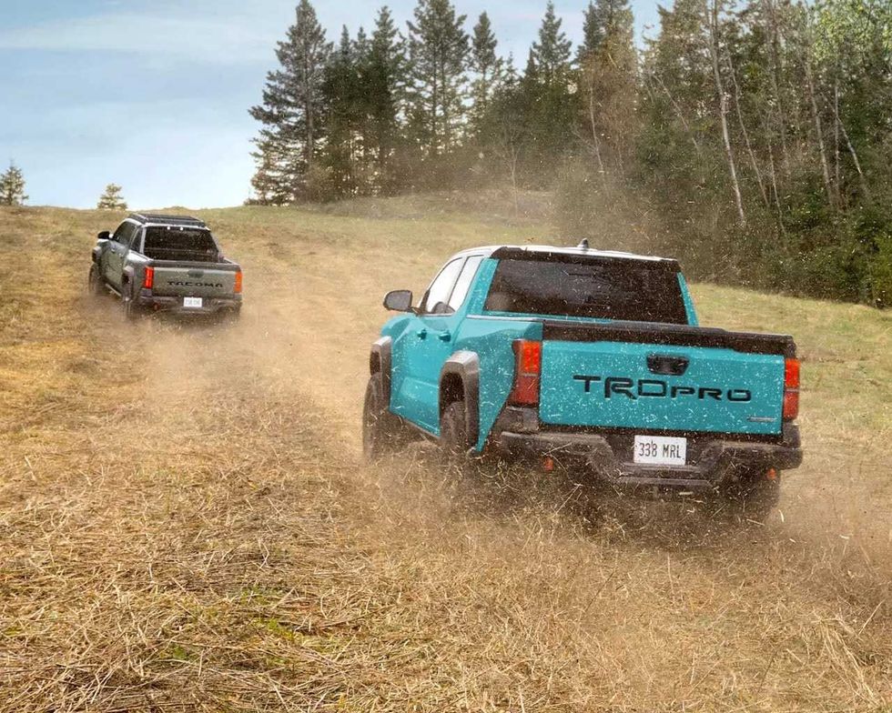 A blue Toyota Tacoma TRD Pro climbs a grassy hill behind another Toyota truck.