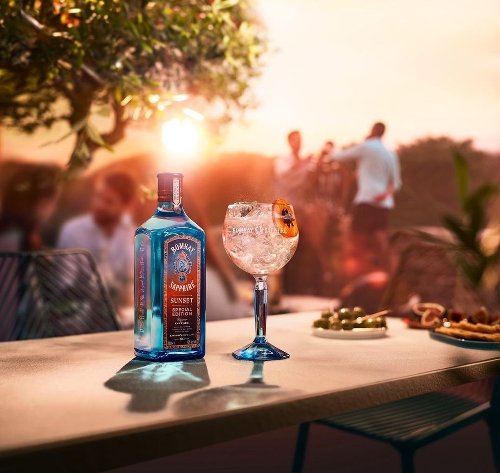 A bottle of Bombay Sunset with a gin and tonic on a patio during sunset.
