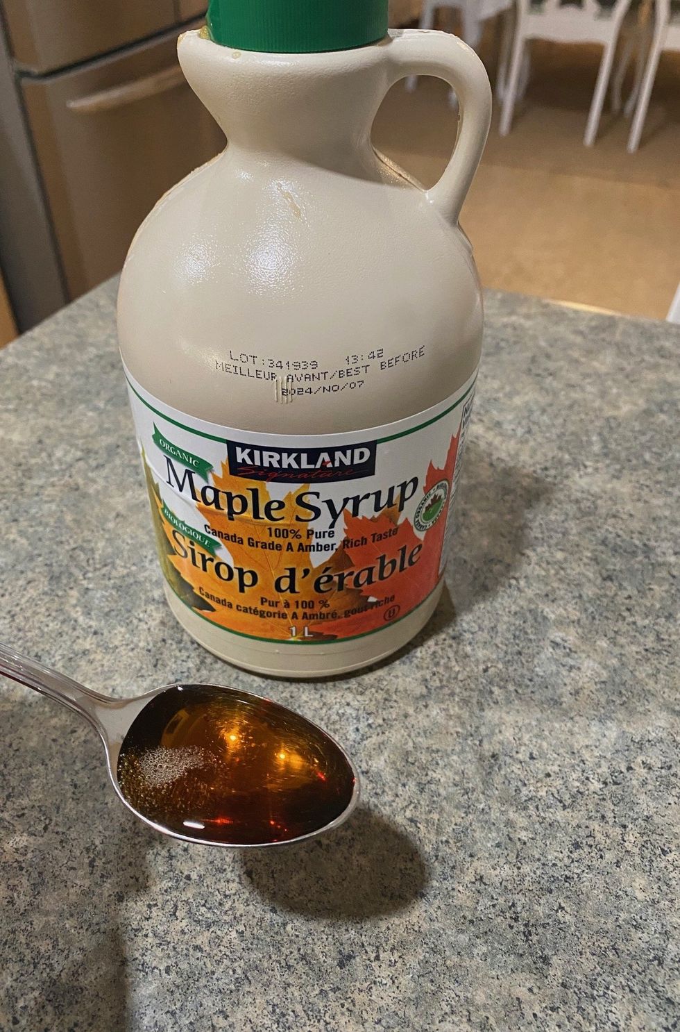 A bottle of Kirkland Signature Organic Pure Maple Syrup and Asymina holding a spoonful of it.