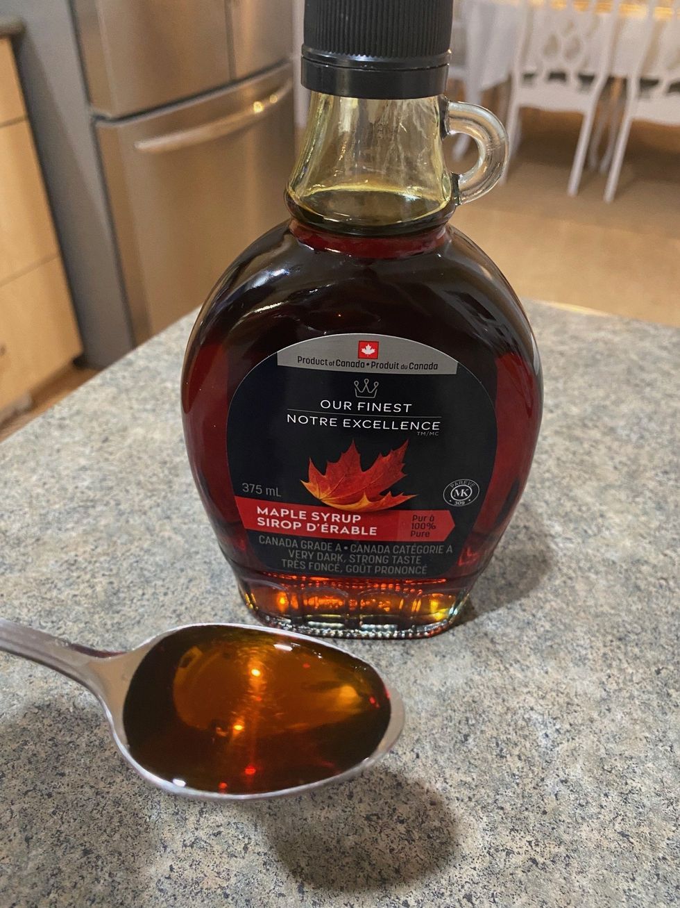 A bottle of Our Finest Maple syrup with syrup on a spoon.