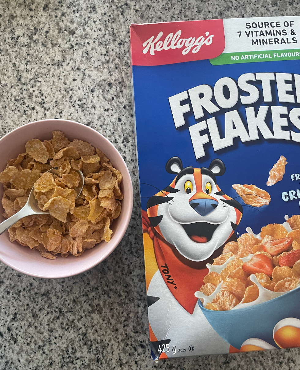 A bowl of Frosted Flakes with the cereal box beside it.