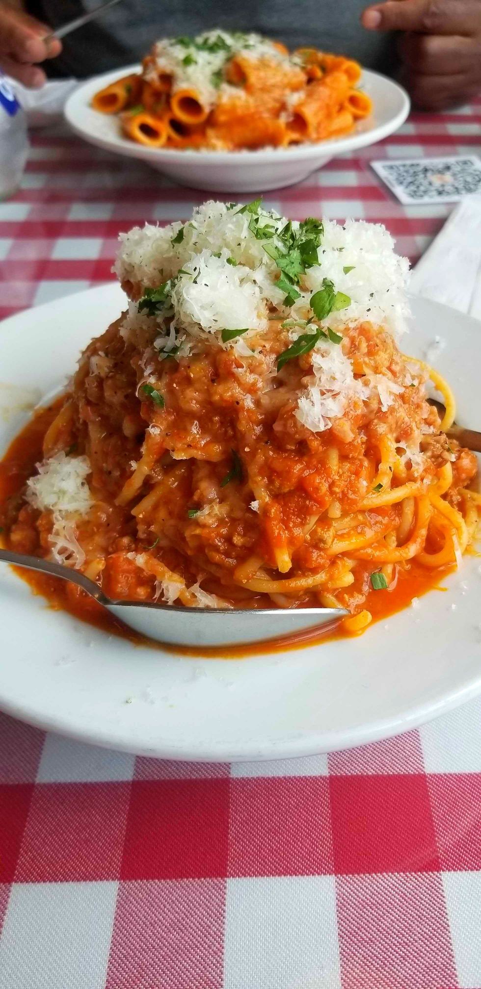 A bowl of spaghetti from Sugo on a red checkered table cloth.