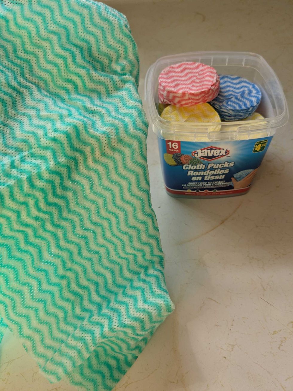 A box of cleaning pucks and one that has been wetted and opened into a green cloth on the counter