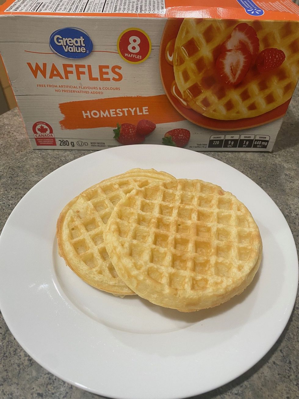 A box of Great Value frozen waffles and two toasted waffles on a plate.