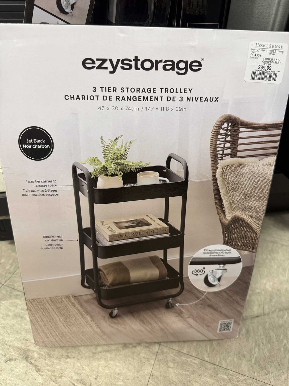 A box with a picture of a black storage trolley with books, plants and a blanket on it in a store.