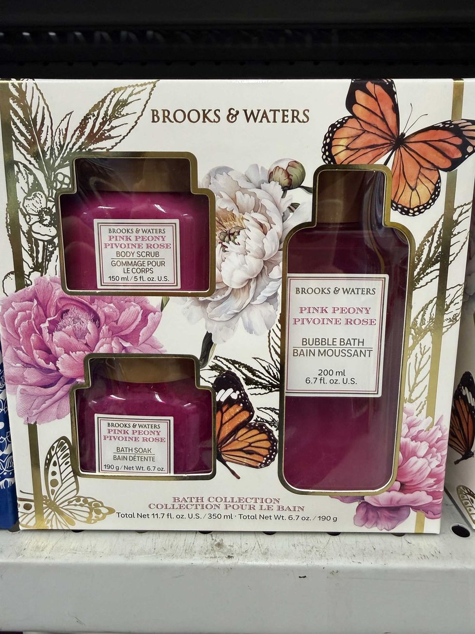 A box with flowers and butterflies on it and three pink bottles inside containing bubble bath, body scrub and bath soak.
