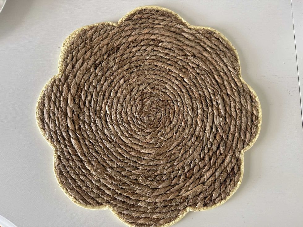 A braided flower-shaped placemat with a yellow trim around it on a white dining table.