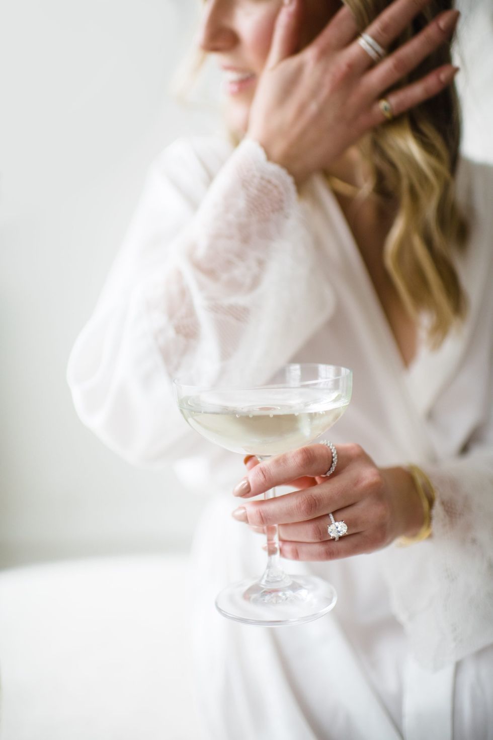 A bride-to-be wearing an oval engagement ring and holding a glass of champagne.