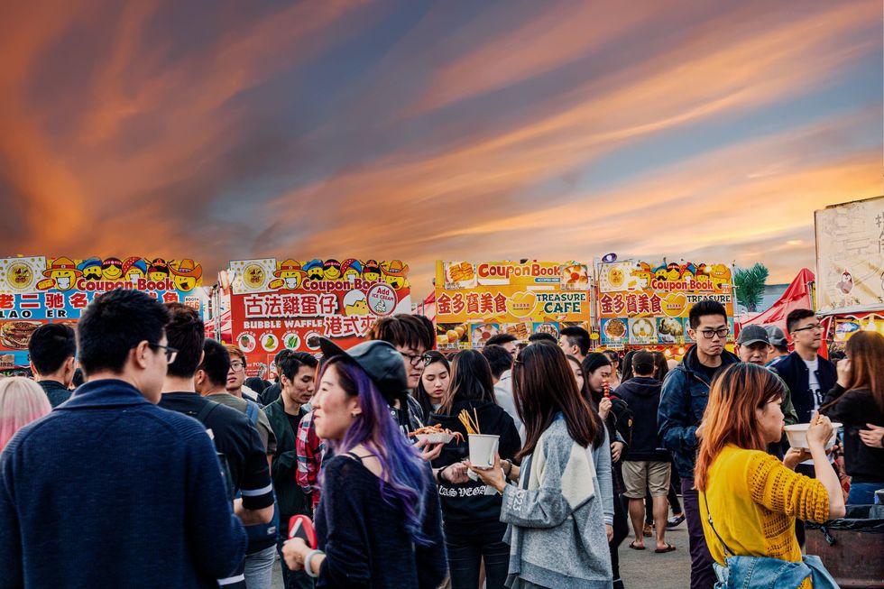 A bustling crowd eating different food outside a row of food stalls during sunset at Richmond Night Market. 