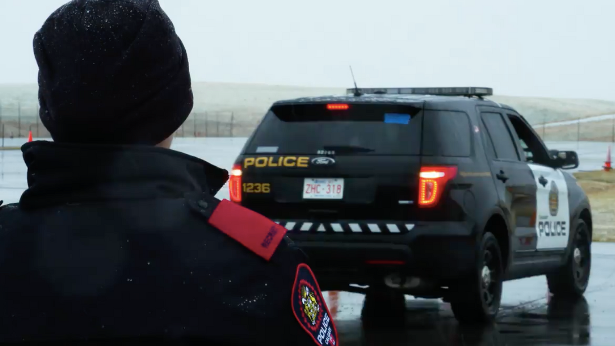 A Calgary police officer looks towards a police car.