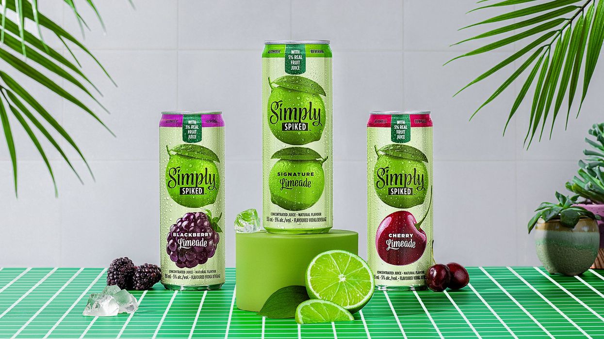 A can of each of the three flavours of Simply Spiked Limeade arranged on a green tiled table with fresh lime, cherry and blackberries.