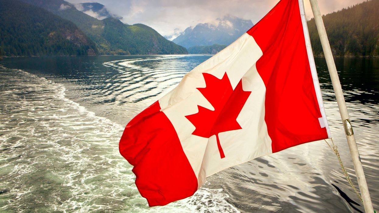 A Canadian flag by the water with mountains in the background.