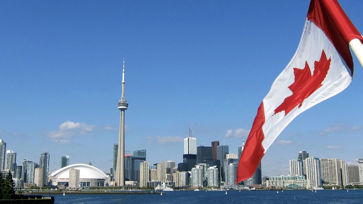 A Canadian flag with Toronto's skyline in the background.