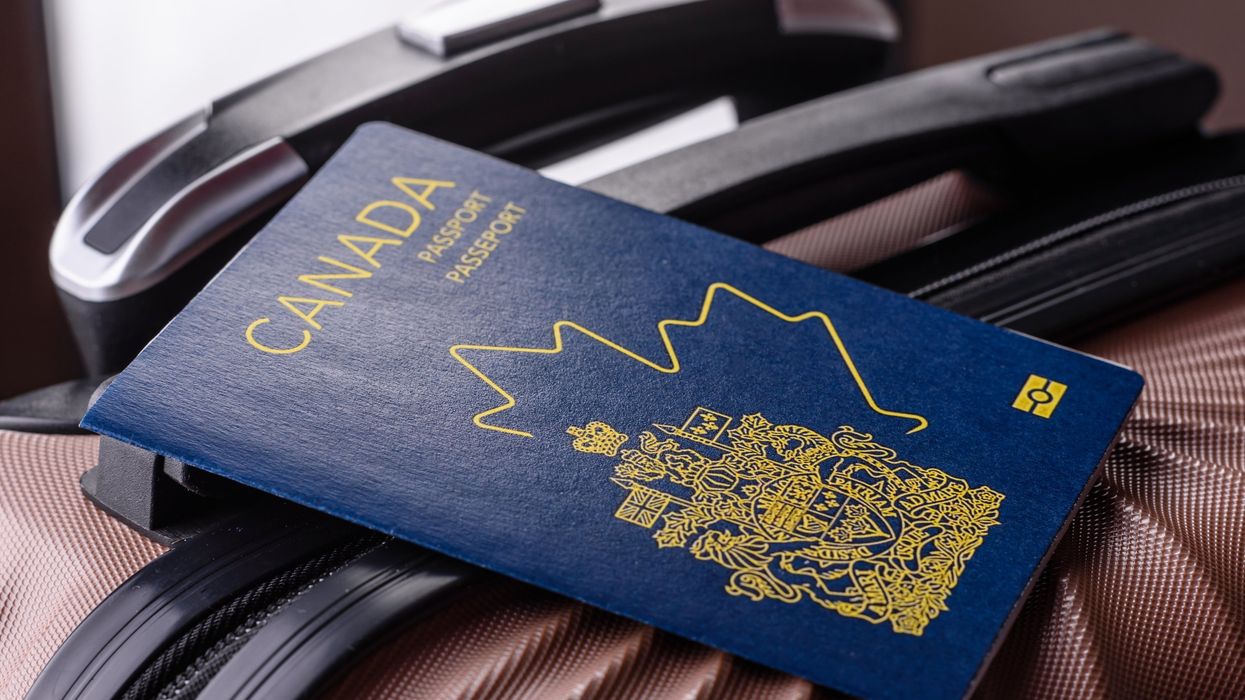 A Canadian passport resting on top of a pink hard-shell suitcase, with a black handle visible in the background.