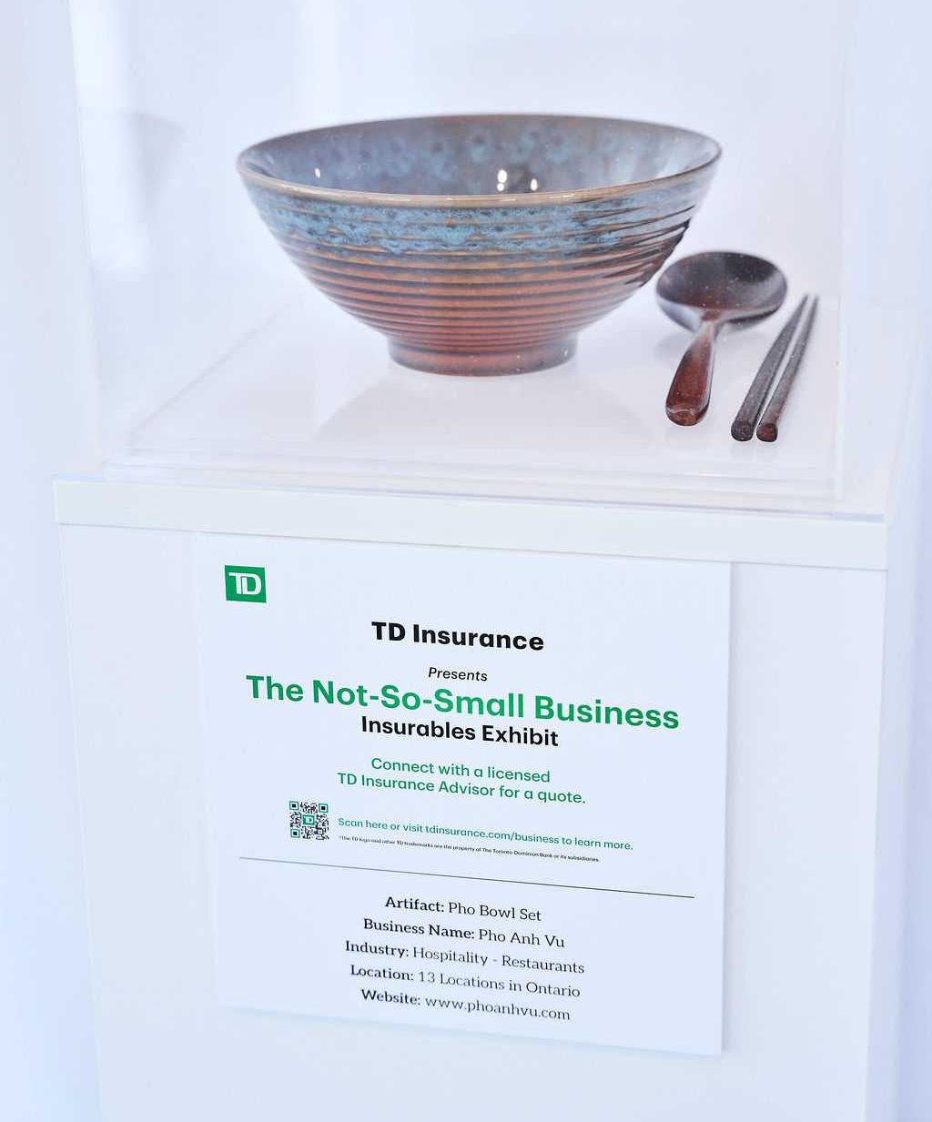 A ceramic bowl, a spoon and chopsticks displayed on a pedestal with a sign that explains it's from Pho Anh Vu Vietnamese restaurant