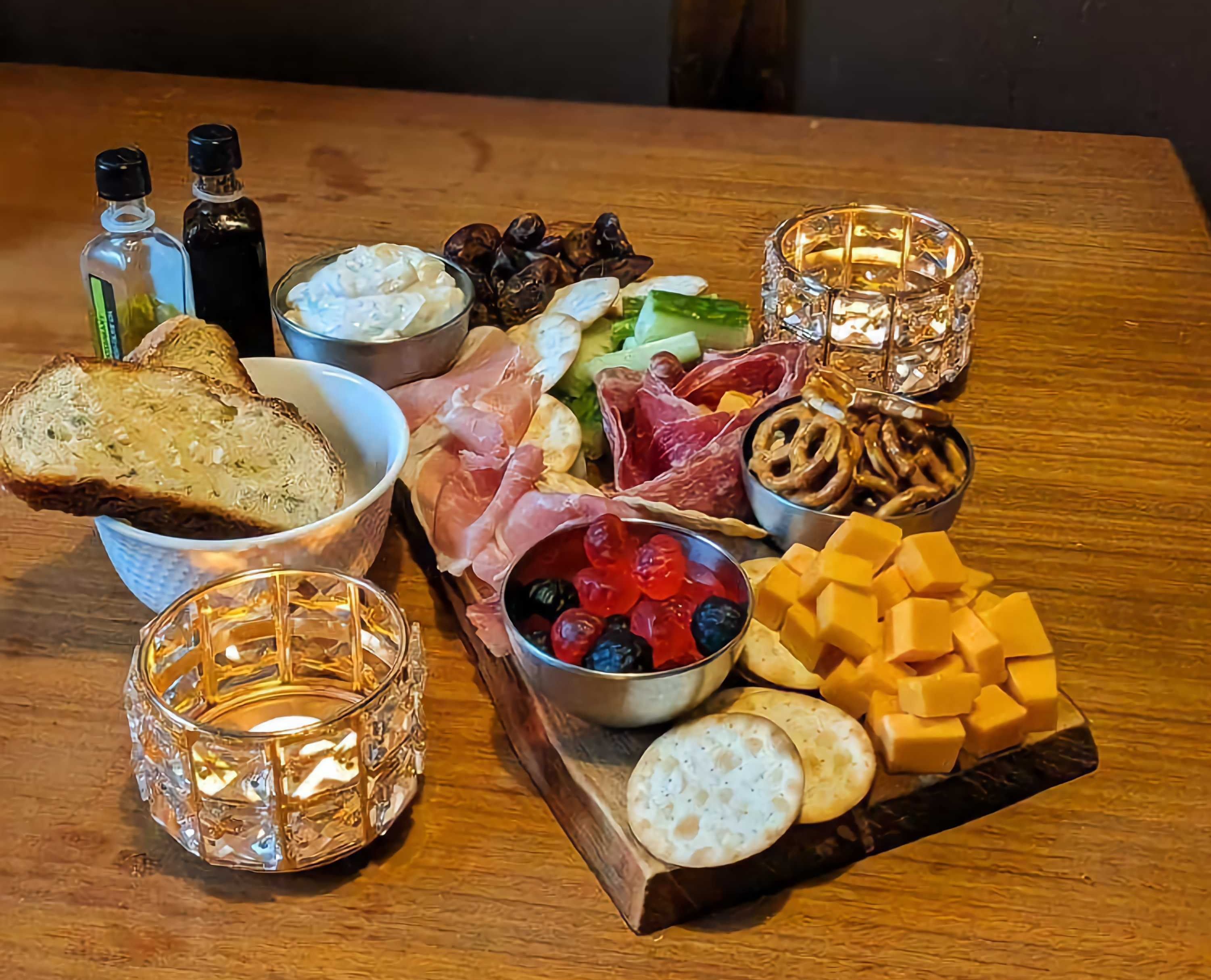 A charcuterie board with crackers, cheddar, sour cream dip, berry candies, dates, deli meat, cucumber and pretzels. \u200b