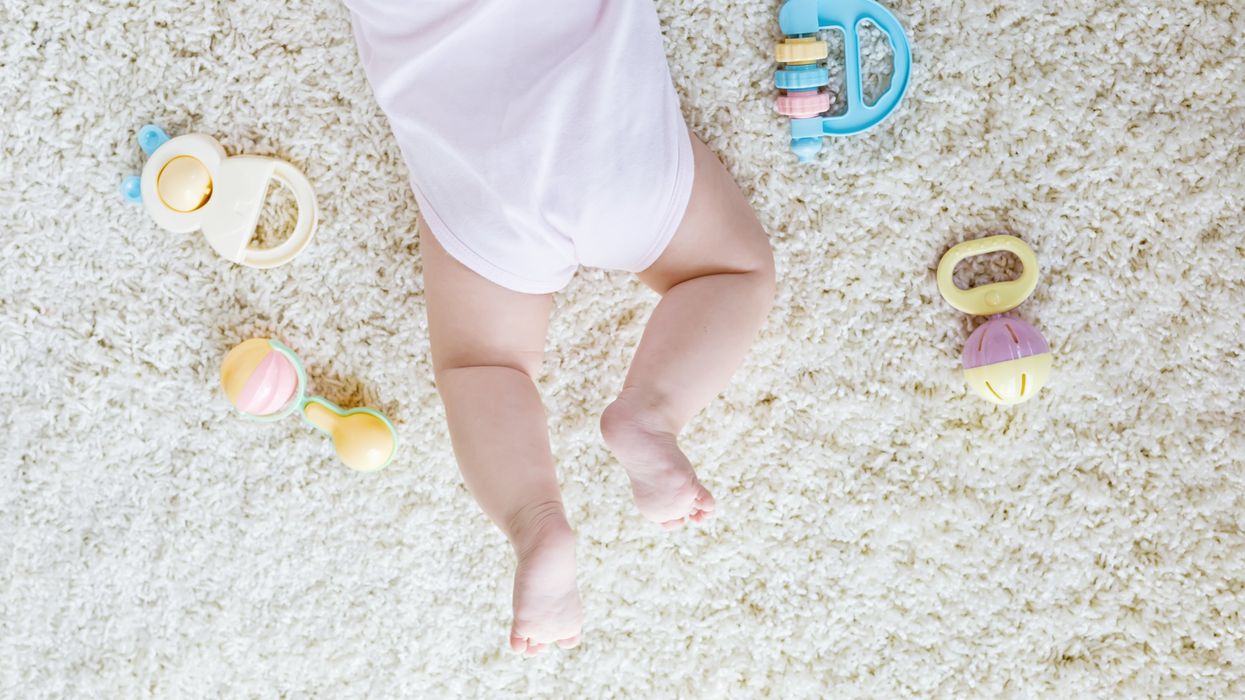A child lies on a fluffy carper, surrounded by colourful rattle toys.