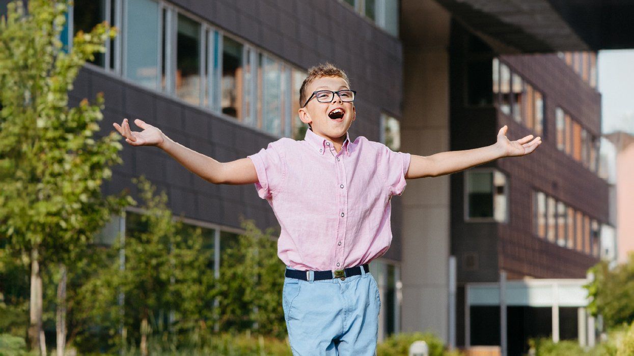 A child wearing a pink shirt and blue trousers, smiling with arms outstretched.