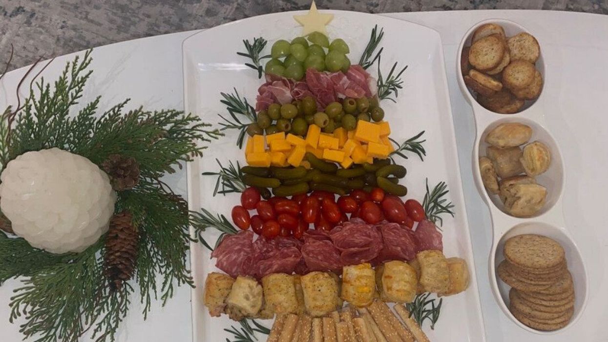 A Christmas-themed charcuterie board on a coffee table with a pine-one shaped candle next to it and bowls of crackers.