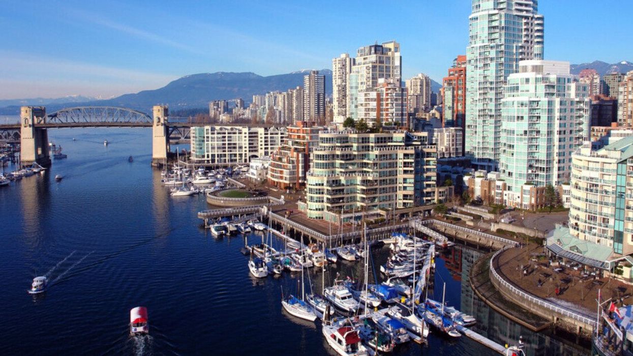 A city skyline filled with tall buildings, boats in the harbour, a bridge and mountains in the background.