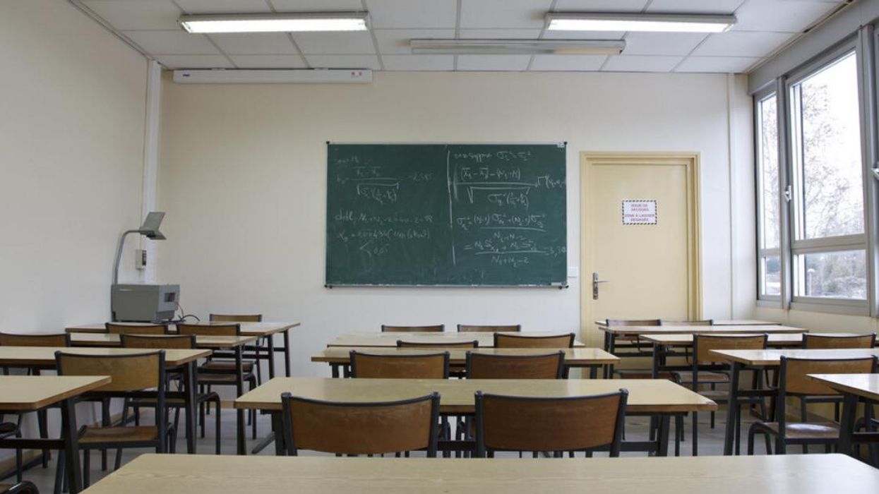 A classroom with a chalkboard, tables and empty chairs.