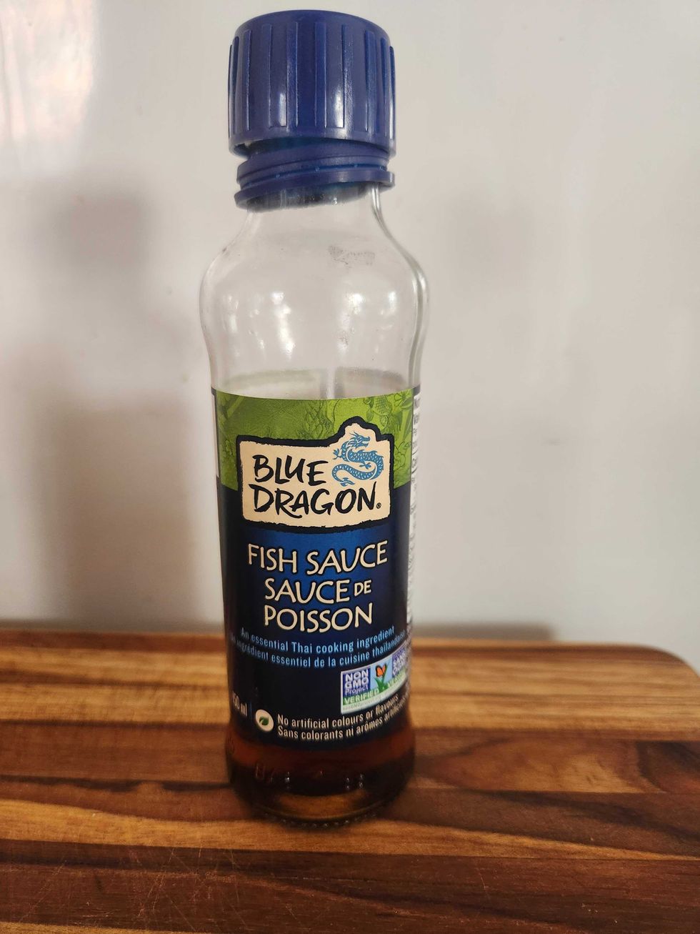 A clear bottle with a blue label on a wood cutting board.