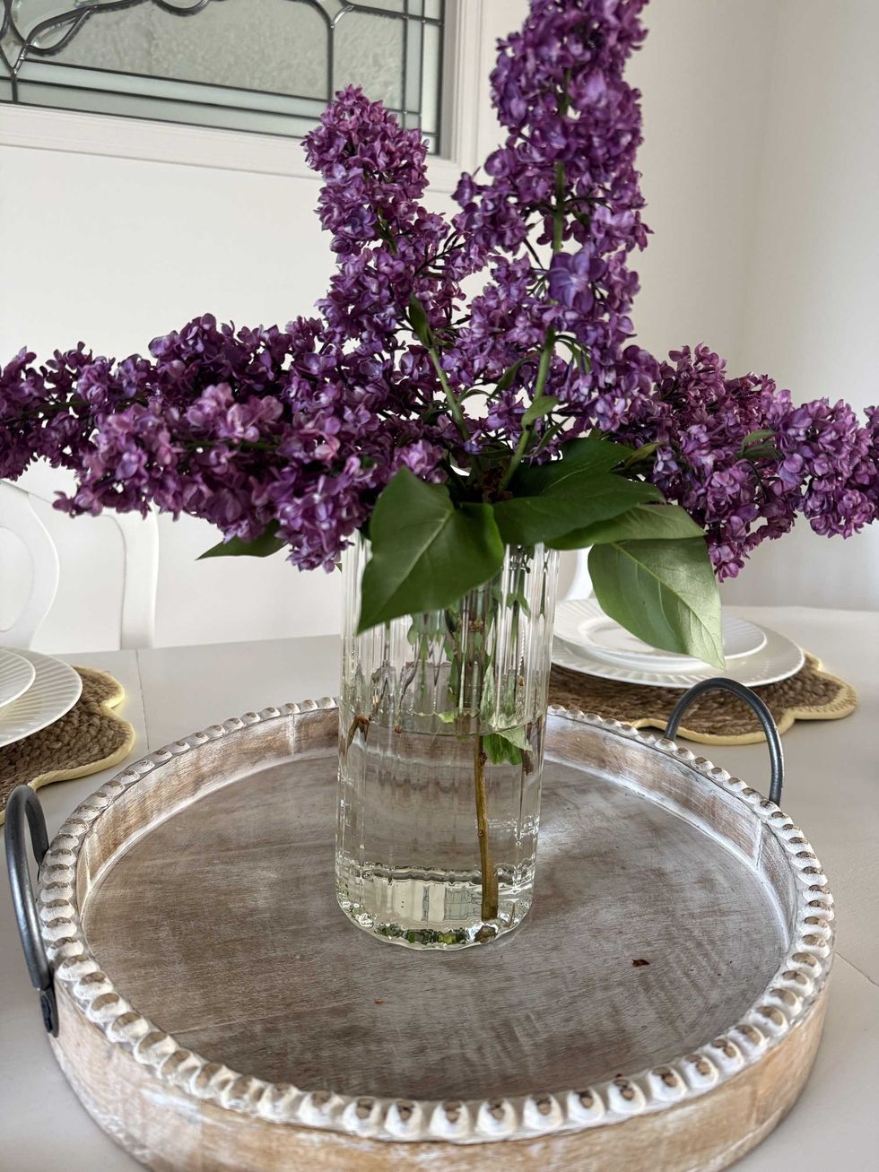 A clear glass vase with purple flowers sitting inside on a dining table.