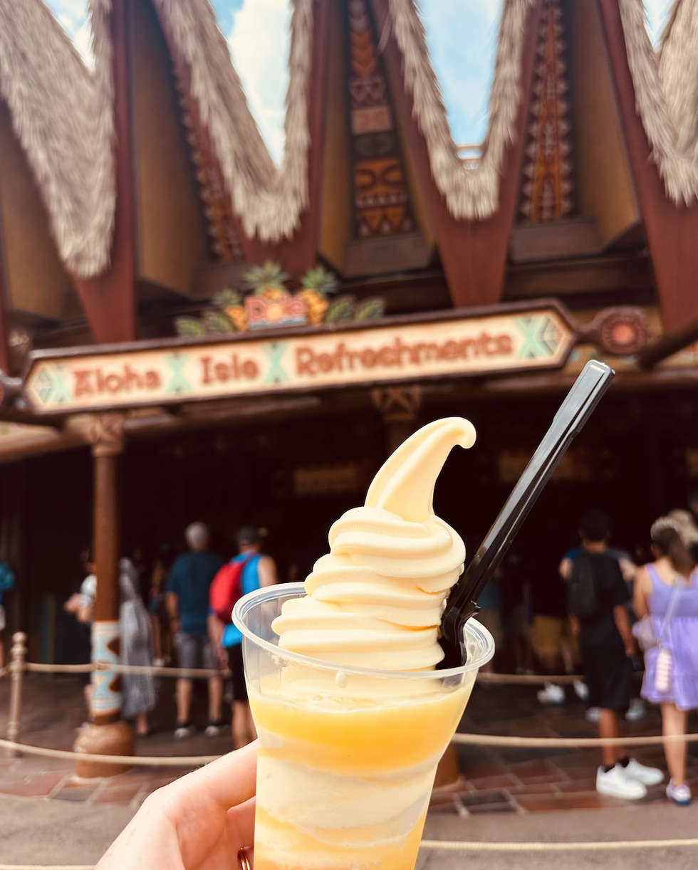 A close-up of a Dole Whip dessert held in front of the Aloha Isle Refreshments stand at Disney World.