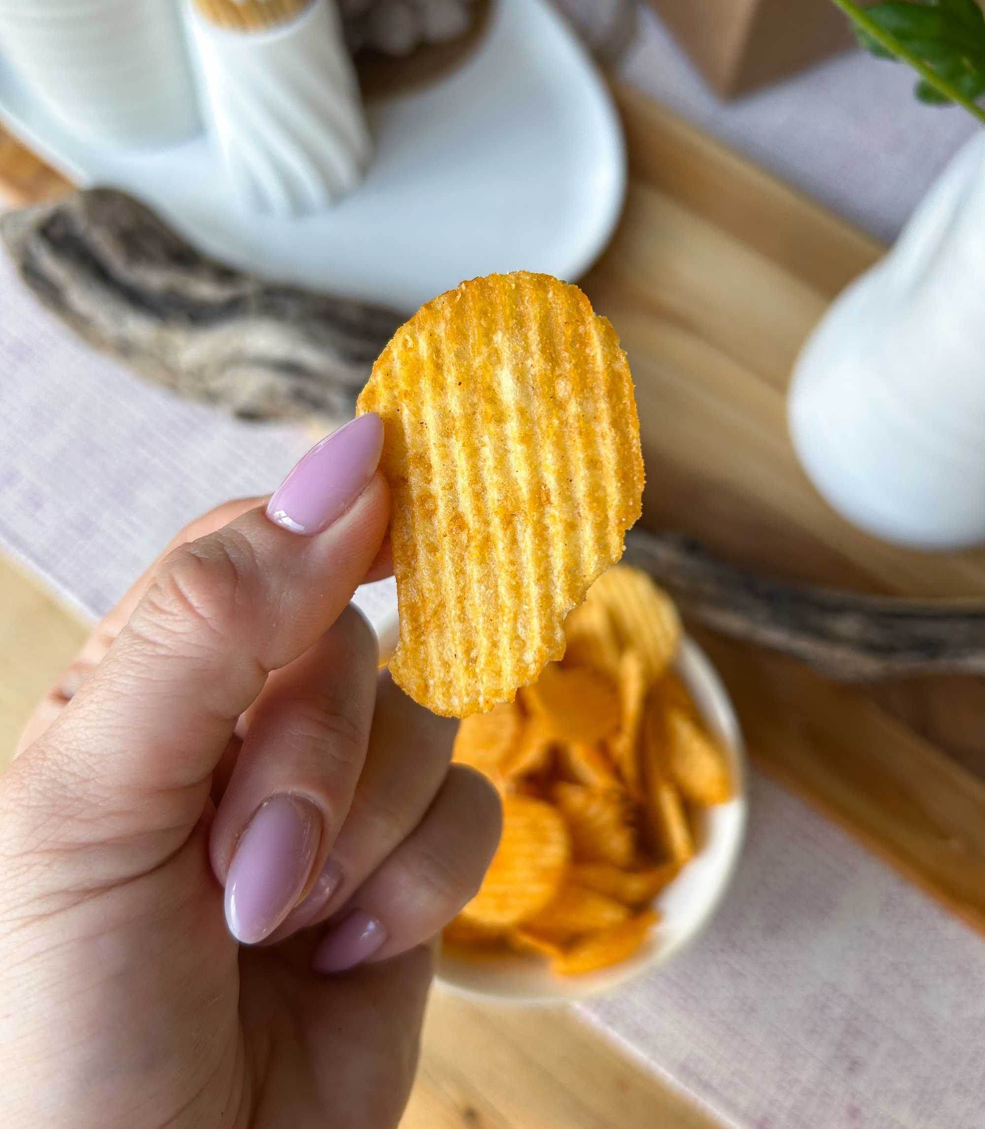 A close up of a person holding a ruffled chip between their fingers