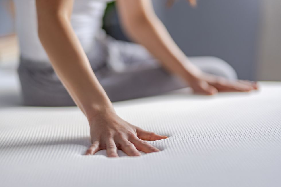 A close up of a person's hands pressing gently onto the surface of an Emma Sleep mattress demonstrating its softness.