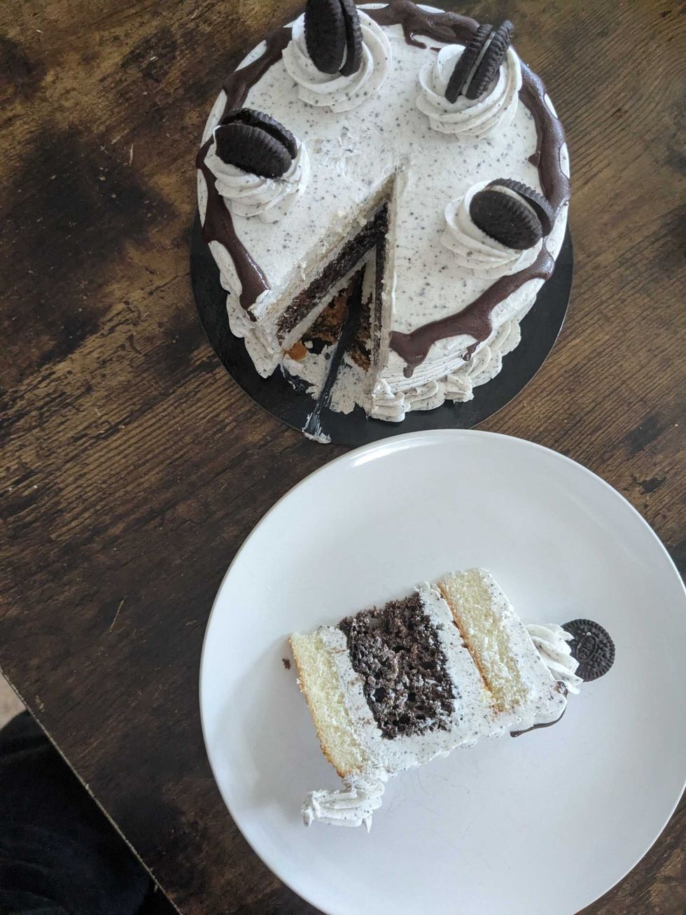 A cookies and cream cake with a slice taken out and on a plate next to it.