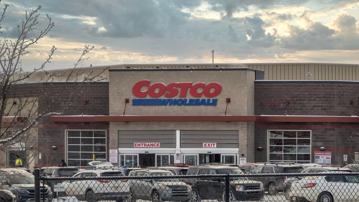 A Costco Wholesale warehouse with a packed parking lot on a cloudy winter day.