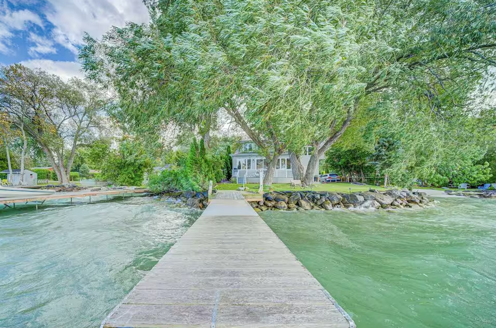 A cottage is seen on an island surrounded by water with a boardwalk leading to it.