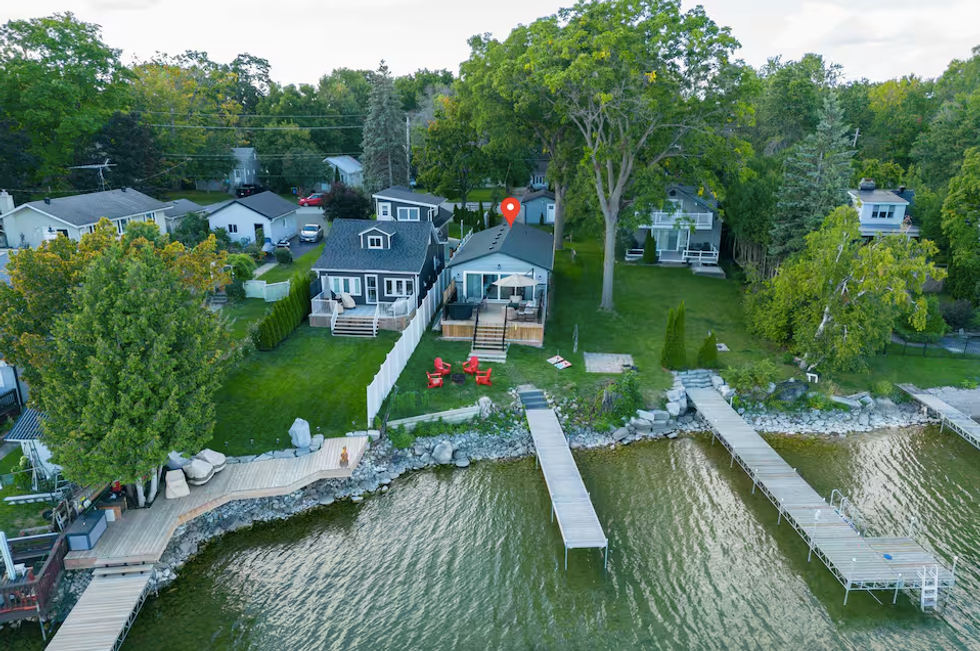 A cottage is seen on the edge of a lake, with a boardwalk leading out to the water.