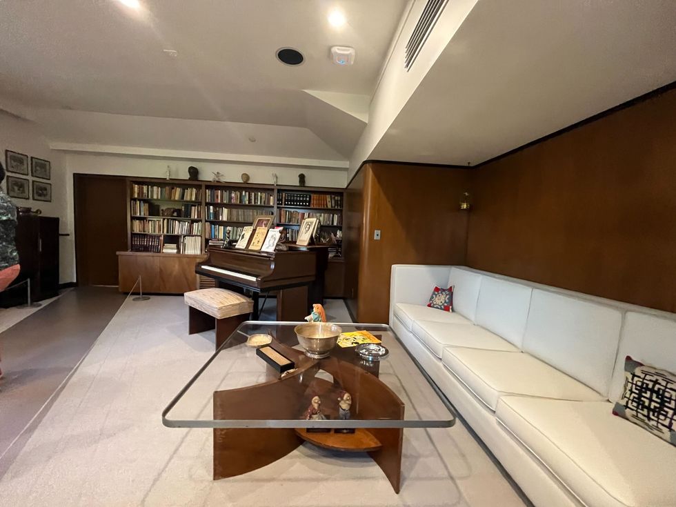 A couch, coffee table, piano and bookcase full of books.