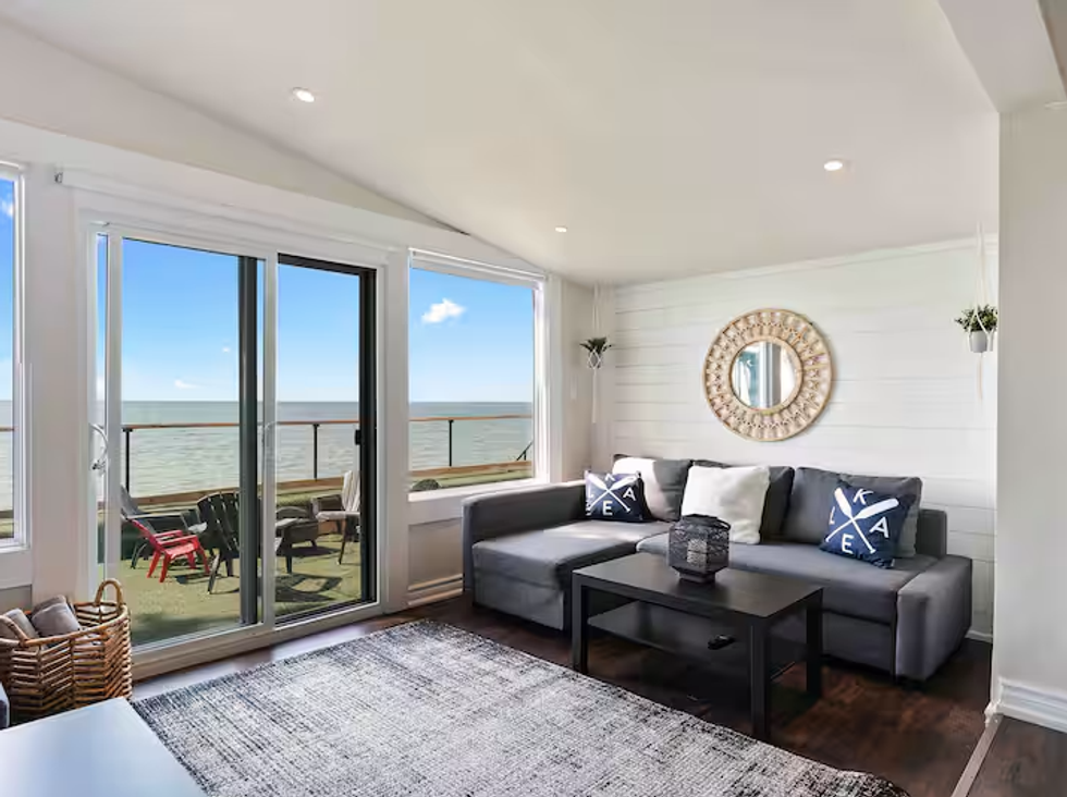A couch is seen in a white living room with a window looking out on a lake.