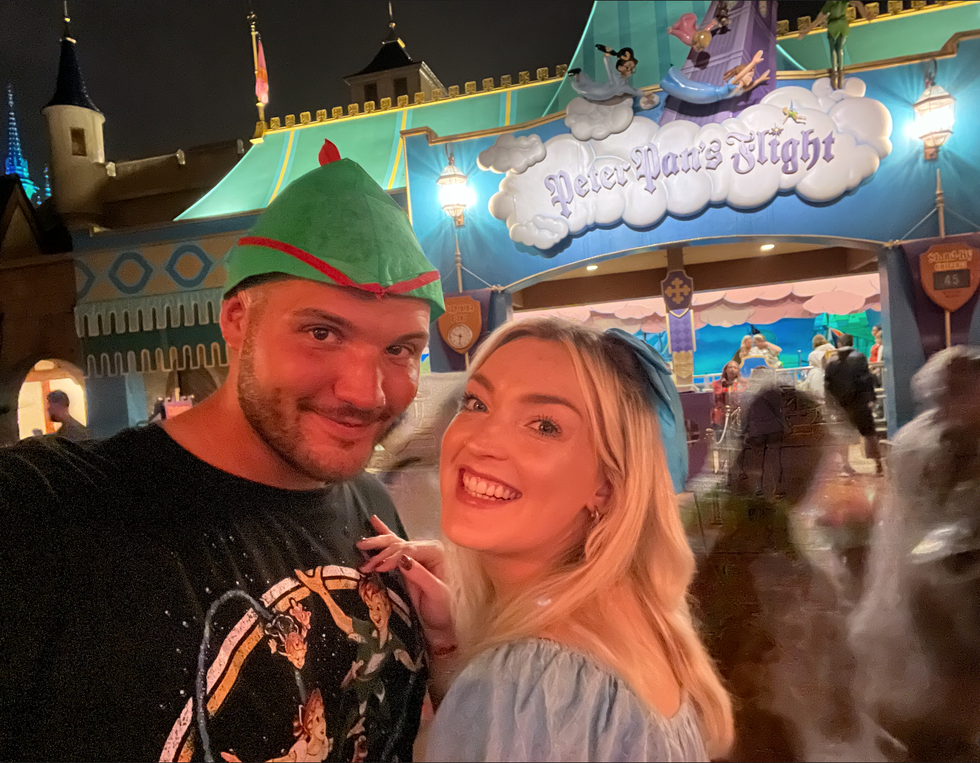 A couple dressed as Peter Pan and Wendy smiling outside the entrance to the Peter Pan's Flight ride at Disney World.