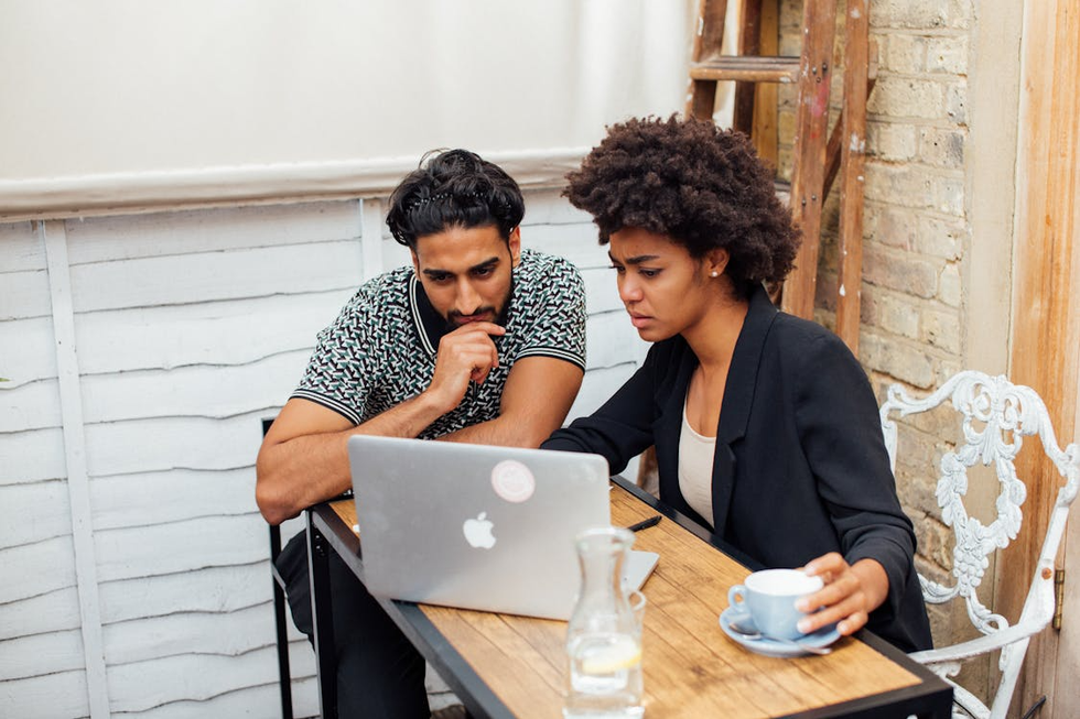 A couple in a rustic cafe look concernedly at a laptop.