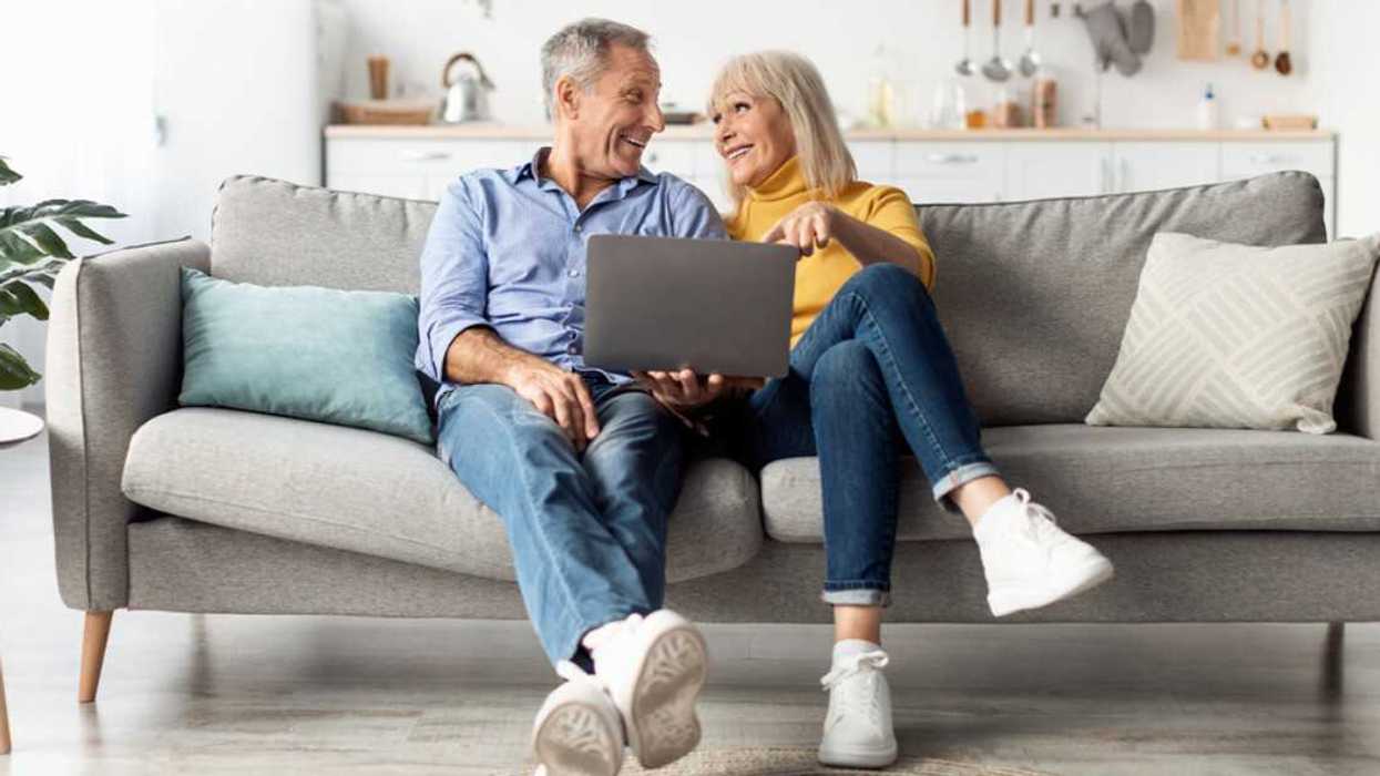 A couple sitting on a couch looking at a laptop.