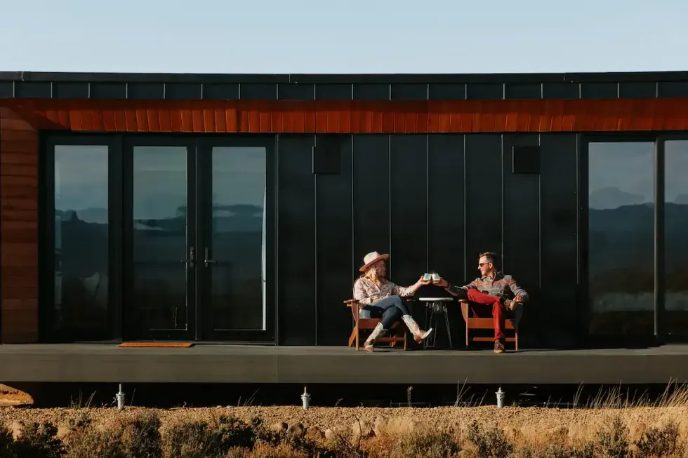 A couple sitting on the deck of the "Taos Skybox Stargazer High Desert Retreat" Airbnb in El Prado, NM.